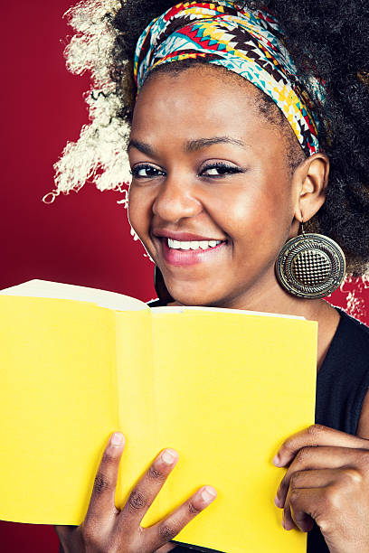 istock Smiling woman with Afro holds yellow book  offering copy space 175194286