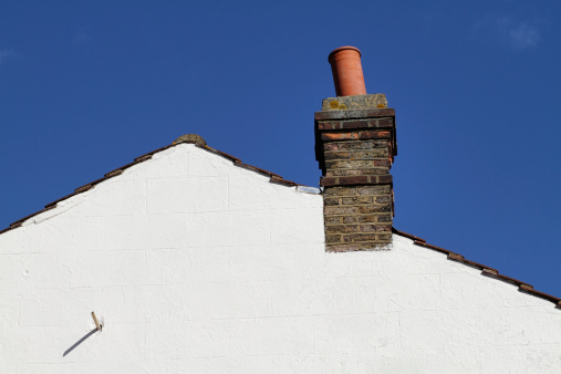 White-painted triangle shape of a pitched-roof gable end, with an old, leaning chimney and water overflow pipe. It was built in about 1900. Surrey / Greater London, England. There is space for copy on the white bricks and in the blue sky. Bricks for background patterns: .