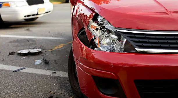 Photo of A red car with a damaged headlight after an accident