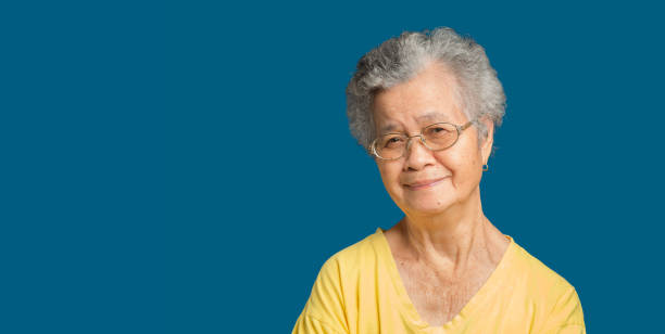 istock Elderly Asian woman looking at the camera with a smile while standing on a blue background 1751951555