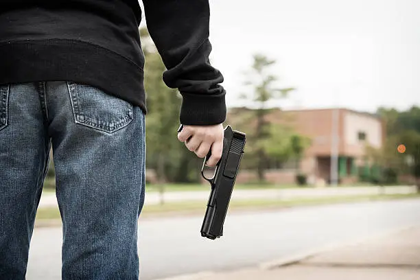 A student wearing jeans and a black hoodie stands outside of school holding a gun.Similar Images: