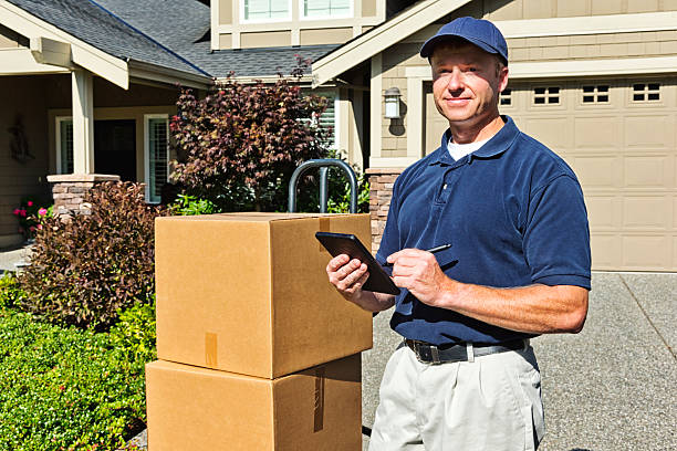Delivery Man with Boxes and Tablet Photo of a delivery man with cardboard boxes on hand truck, holding an electronic signature/trackiong pad. mover delivery person box hand truck stock pictures, royalty-free photos & images