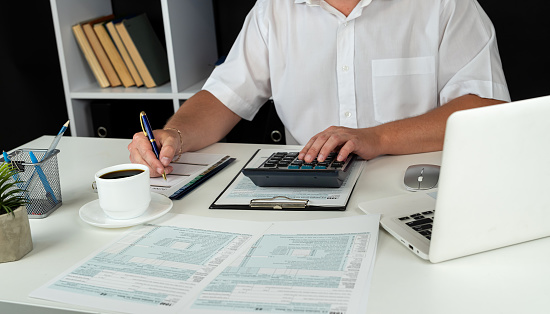 man hand using calculator for accounting  individual income 1040 tax form. April season to pay tax