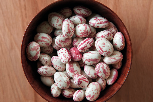 Cranberry beans. Borlotti bean pods in bowl. Top view. Stylish modern food background. Magenta color. Creative foodstuff flat lay. Grocery, dietary backdrop. Advertising, trendy magazine publication. Raw dry red bean. Crimson beans. Snap. White red pods.