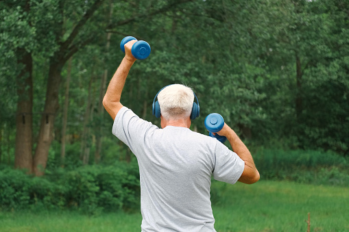 Senior man working out outdoors. Person lifting dumbbells. Old male exercising at park. Healthy people lifestyle. Active sport training. Older elderly sportsman doing fitness exercise. Workout session. Boomer. Old elderly man in sportswear training doing weight lifting dumbbell exercising. Leisure healthy lifestyle. Older male is working out. Fitness for seniors. Active retired people. Mature senior man doing gymnastics. Concept of fitness, recreation, well being, fit. Elderly male exercising training, stretching. Old man energy working out, practice. Retiree person. Sportive Grandpa pensioner on nature background. Cinematic shot. retired working out