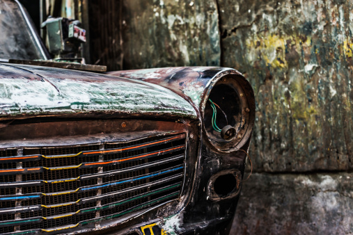 Close-up shot of old rusty car with no headlight and damaged paint.