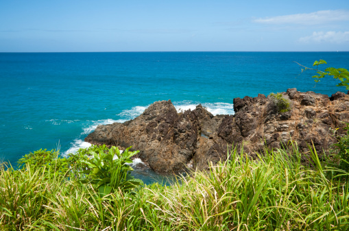 A view of the Caribbean Sea with a large rock along the shoreline and blue waters in the distance.