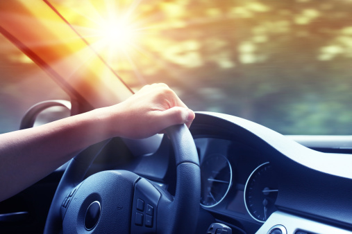 Close-up of a hand on steering wheel in a car, driving under sunset nature background.