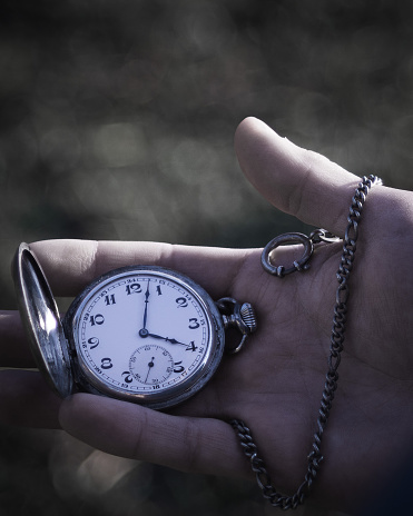 close up of a hand holding a pocket watch with chain, blurred background and desaturated colors
