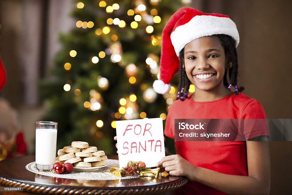 Cookies and milk for Santa. Cute African-American girl wearing Santa's hats prepared cookies and milk for Santa Claus. African Ethnicity Stock Photo