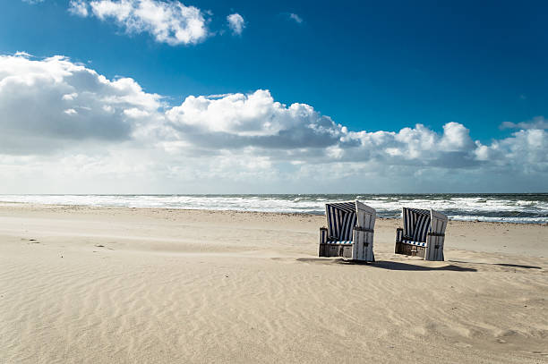 Hooded Beach Chairs Empty hooded beach chairs at the the coastline of the island Sylt - Germany. Copy space on the blue sky in the background. german north sea region stock pictures, royalty-free photos & images