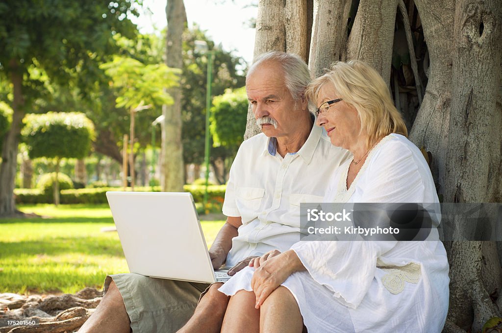 Starsza para działa na laptopie w parku - Zbiór zdjęć royalty-free (50-59 lat)