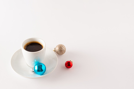 Cup of coffee with Christmas decoration balls isolated on white background. Minimal Christmas morning coffee concept. Copy space.