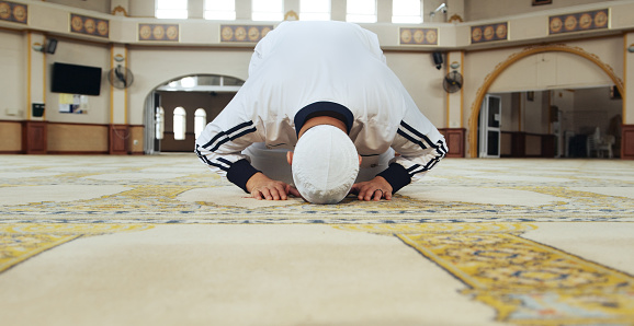 Muslim man, kneeling and praying in mosque for faith, respect or islamic commitment to Allah. Moslem culture, salah and prayer in sujood for spiritual worship, holy religion or trust in God for peace