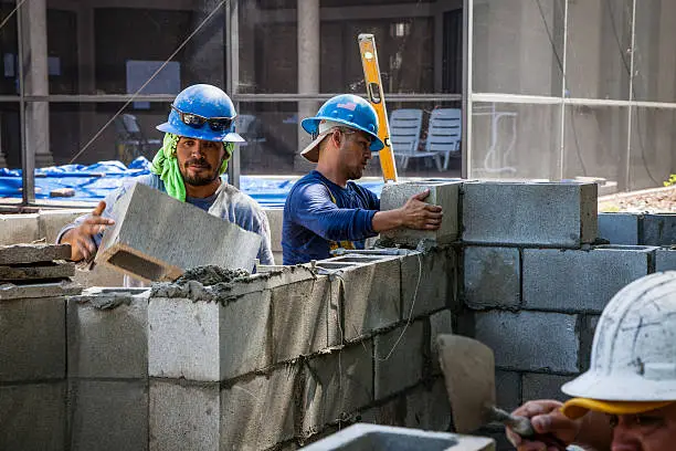 Construction workers at a job site in SW Florida are building a concrete block wall.