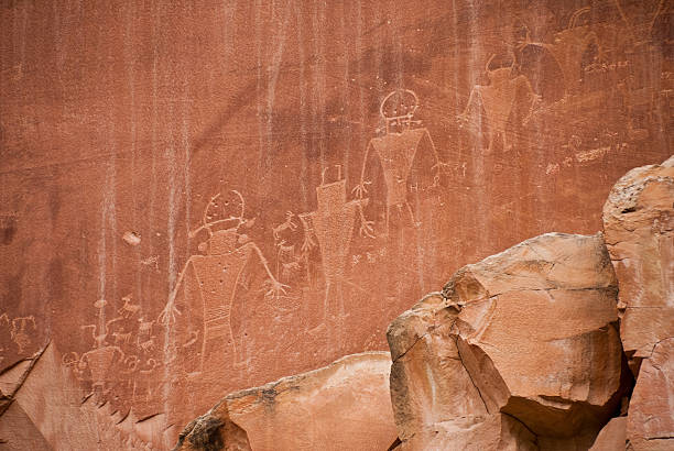 Petroglyphs on the Canyon Wall Capitol Reef National Park is in the desert of southern Utah. The park is filled with cliffs, towers, domes and arches. The first part of the park’s name derives from the many dome shaped Navajo Sandstone formations each of which resembles the US capitol. The second half of the name refers to the parallel impassable ridges which the early settlers called reefs. The first paved road through this area wasn’t constructed until 1962. Central to the area is the famous Waterpocket Fold, a 100-mile wrinkle in the earth, which is 65 million years old and the largest exposed monocline in North America. The Fremont River has carved canyons through some parts of the Waterpocket Fold but the area remains a dry desert. The park is also a showcase for ancient history and the more recent history of the Mormon pioneers. This scene of ancient petroglyphs was photographed in Capitol Reef National Park near Fruita, Utah, USA. jeff goulden capitol reef national park stock pictures, royalty-free photos & images