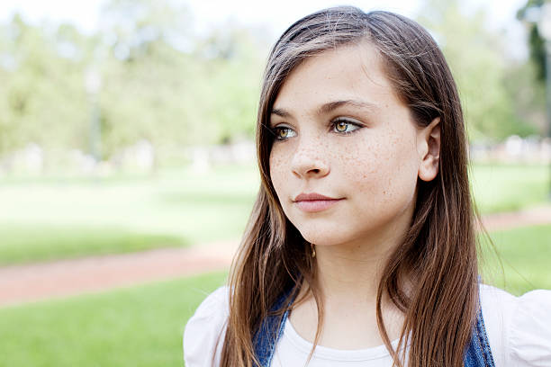 Close-up portrait of a thoughtful young girl with freckles, holding her hands together under her chin, conveying a sense of contemplation or mild concern