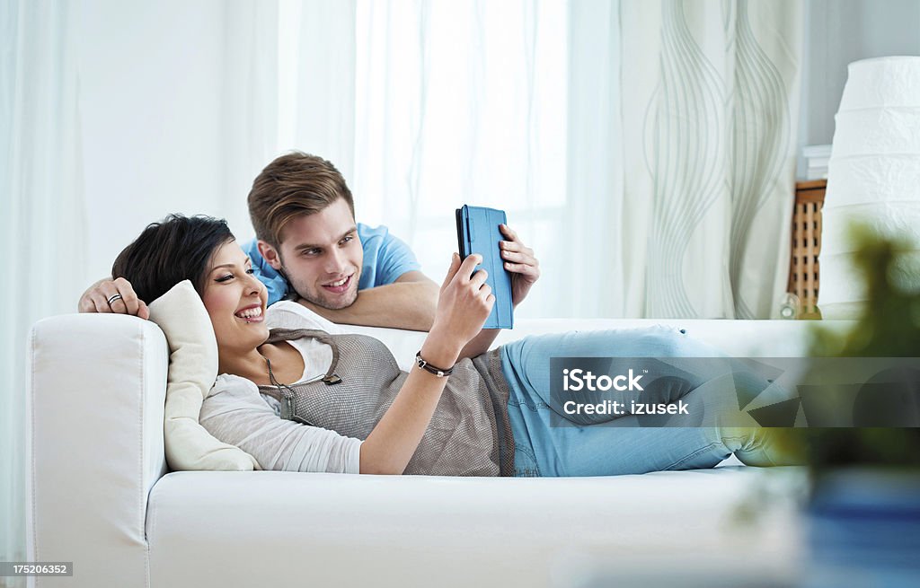 Young couple using e-reader Happy young adult couple using e-reader at home. 20-24 Years Stock Photo
