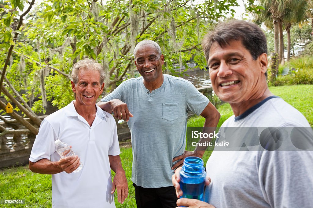 Men in park after exercising Three men standing next to each other in the park, sweating after exercising.  They are all wearing athletic gear, and two of the men have water bottles, and the other man is leaning on one of them. They are all smiling. Mature Men Stock Photo