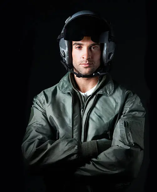 Mid-length of an airforce pilot crossing his arms and wearing a helmet while isolated on black