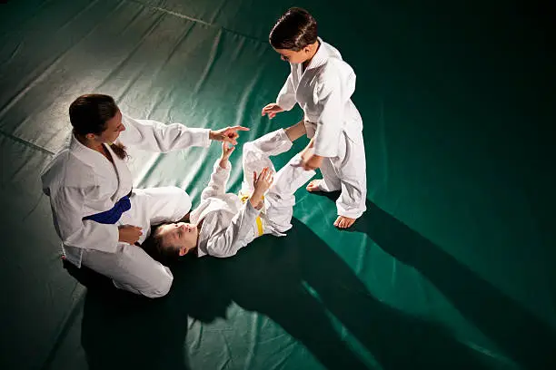 Jiu-Jitsu class - Instructor (20s) teaching students (5-7 years) Open Guard position.  Brazilian jiu-jitsu is a martial art, self defense system and combat sport.