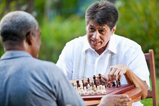 Multi-ethnic men playing chess outdoors.  Focus on Hispanic man (50s).