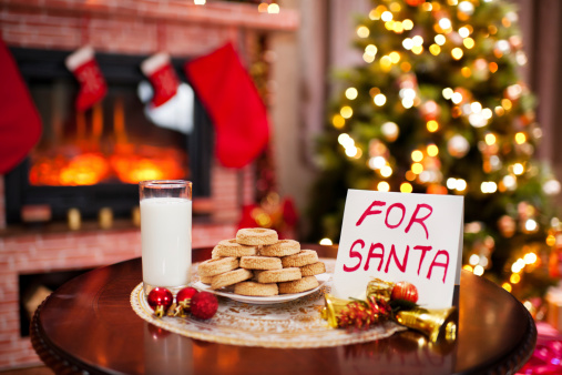 Cookies and milk with a note for Santa. Fireplace and Christmas tree in the background.
