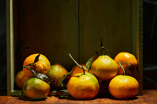 Ripe organic tangerines with leaves in wooden box in bright sunlight with copy space. Natural tropical fruit concept image.