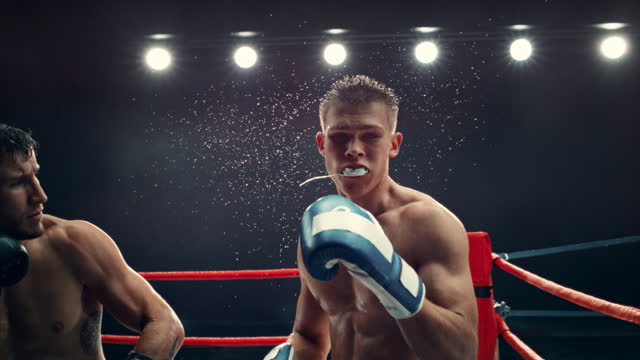 Cinematic Footage with a Speed Ramp Super Slow Motion Effect. Two Professional Boxers Fight in a Ring. Boxer Ducking to Avoiding a Hit, Punching with a Hook to the Face, Rocking the Opponent