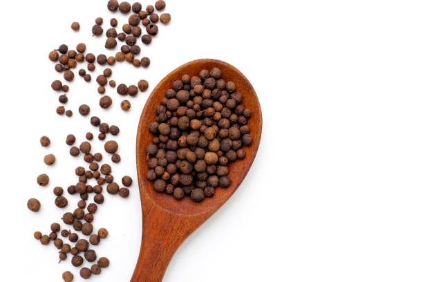 A top-down view of aromatic spices and dried tea leaves arranged on a white background. The composition features star anise, black peppercorns, and two small ceramic bowls filled with dried tea leaves, creating a minimalist yet elegant food presentation. The scattered elements add an organic feel, emphasizing the rich textures and natural beauty of these culinary ingredients. This image is ideal for use in food blogs, tea packaging designs, spice advertisements, or educational content about traditional herbs and spices.