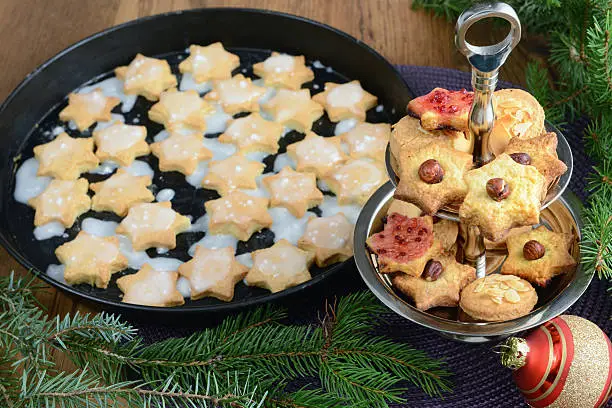 Cake Stand (Etagere) with Christmas sweets like cinnamon pastry and biscuits. In the background another baking sheet with cookies as well as pine green and Christmas balls. Useful as Christmas and Advent greeting card background.
