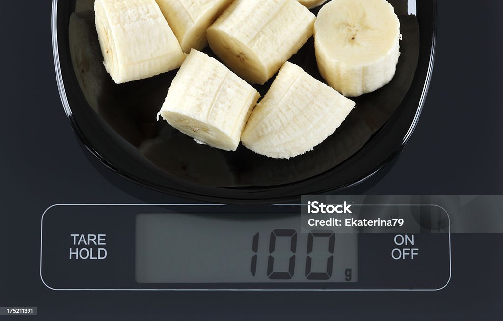 Banana on kitchen scale Peeled sliced aaaabanana in a black plate on digital scale displaying 100 gram. Scale Stock Photo