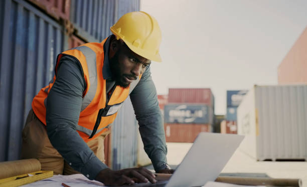 istock Engineering man, computer and warehouse container, blueprint of floor plan at outdoor construction site. Industry contractor, project manager or african person typing on laptop for safety maintenance 1752117505
