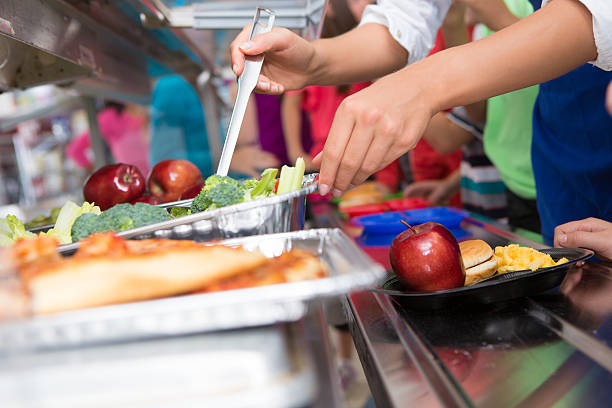 cuoco di mensa aiutando gli studenti elementari selezionare il cibo a pranzo linea - mensa foto e immagini stock