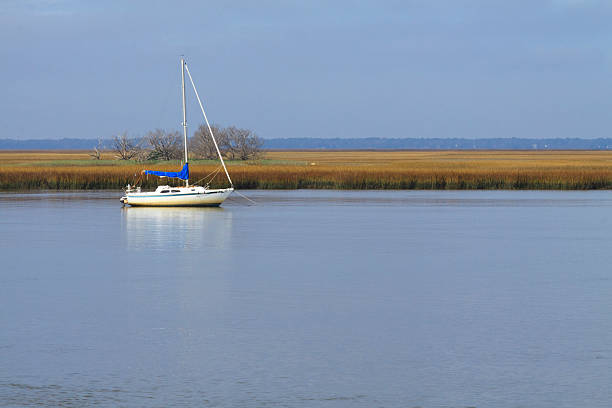 Anchored Sailboat "A horizontal view of an sailboat, anchored in a river of the Georgia Marshes." saint simons island photos stock pictures, royalty-free photos & images