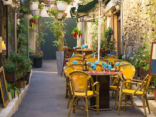 "Narrow street with typical medieval buildings in Aix en Provence town, South France. Tables set for a lunch in front of a restaurante."