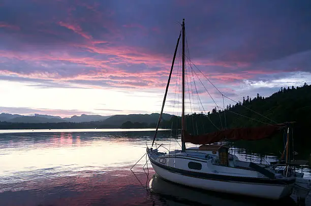 "small sail boat at anchor in the English Lake District, silhouetted against a red setting sun"