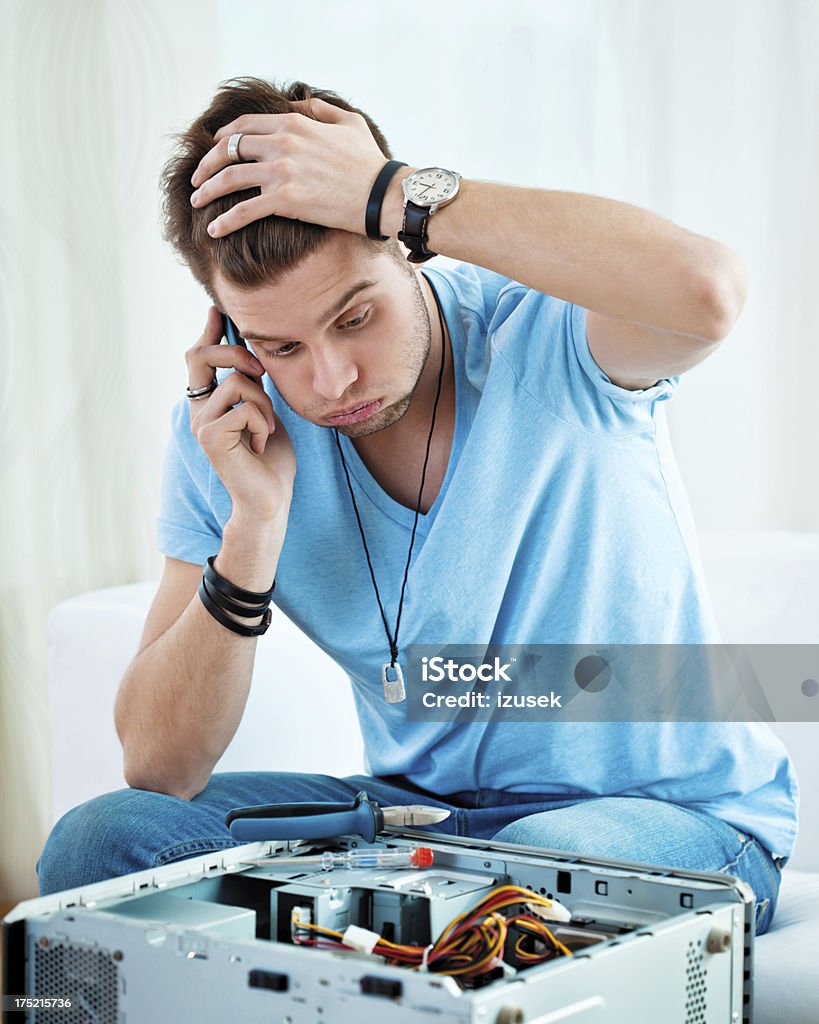 Problem with computer Young man has problem with his computer, trying to reach hotline. Using Phone Stock Photo