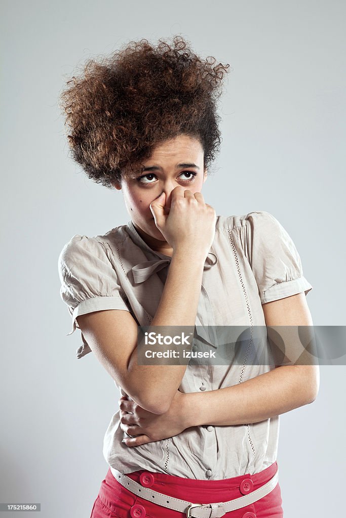 Teen girl pinches nose Portrait of disgusted young woman pinches her nose and looking away. Studio shot, grey background. Unpleasant Smell Stock Photo