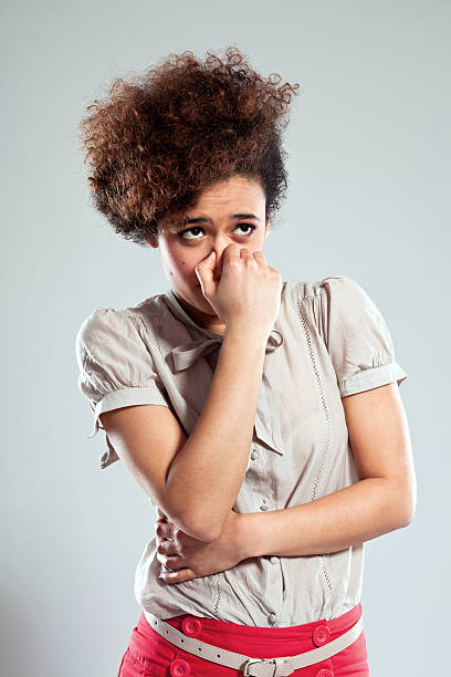 Teen girl pinches nose Portrait of disgusted young woman pinches her nose and looking away. Studio shot, grey background. holding nose stock pictures, royalty-free photos & images