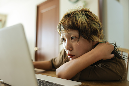 Close up shot of young asian Gen-Z female with colorful hair at a cafe or Home struggling to find work while searching on her laptop. Showing signs of disappointment.