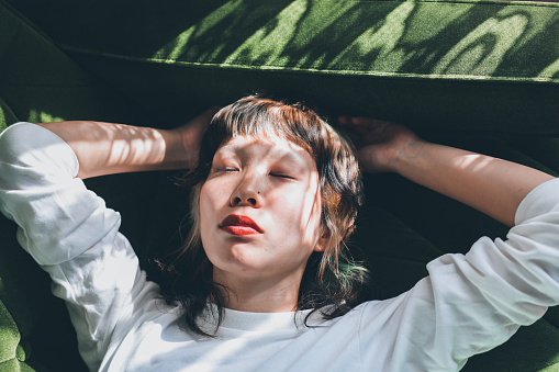 Close up shot of young asian Gen-Z female with colorful hair relaxing on the sofa at home under the sun cast through the window.