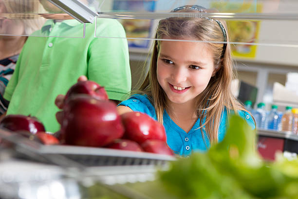 Cute little girl taking apple in school lunch line Cute little girl taking apple in school lunch line. cafeteria school lunch education school stock pictures, royalty-free photos & images