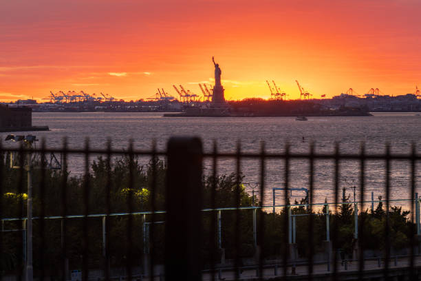 The sun sets behind the Statue of Liberty, shot from Brooklyn, NY