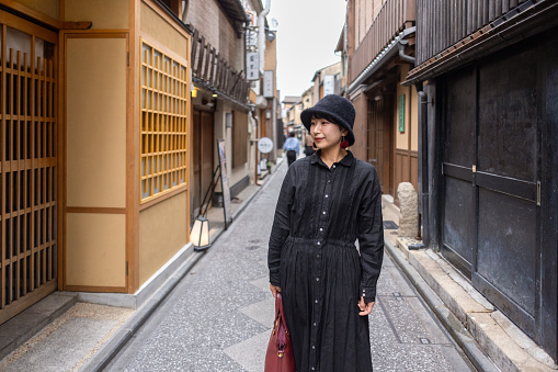 Young woman in black dress with a hat walking in traditional Japanese narrow street