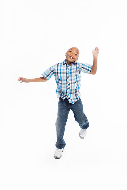 Little smiling boy with dark hair in blue jeans, blue polo t-shirt is jumping and having fun on an isolated white background in a photo studio