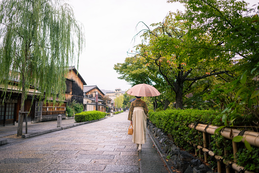 Rear view of young woman in Kimono/Hakama walking on traditional Japanese town in a rainy day