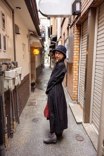 Young woman in black dress with a hat walking on traditional Japanese narrow street