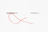 A sewing needle with red string through the white background