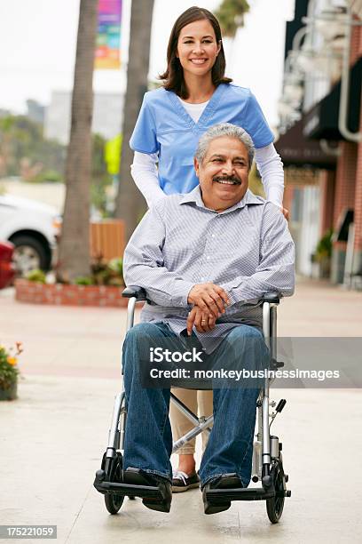 Carer Pushing Disabled Senior Man In Wheelchair Stock Photo - Download Image Now - Latin American and Hispanic Ethnicity, Nurse, Senior Adult